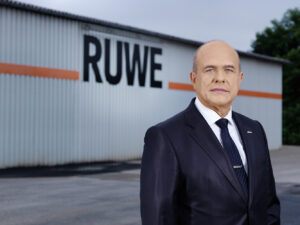 Ein Mann in Anzug und Krawatte steht vor einem Gebäude.